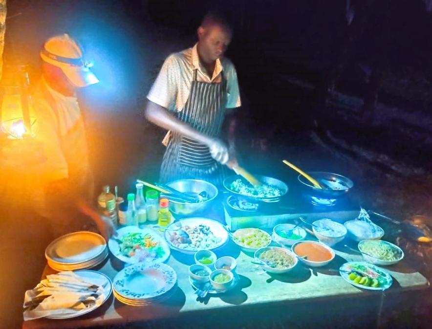 un uomo che prepara il cibo su un tavolo con ciotole e piatti di JozaniBiospherevillage a Jozani