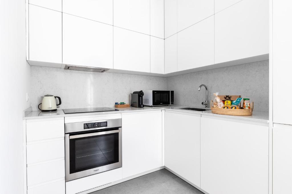 A bright white kitchen includes an oven, sink, kettle, coffee maker, and microwave.