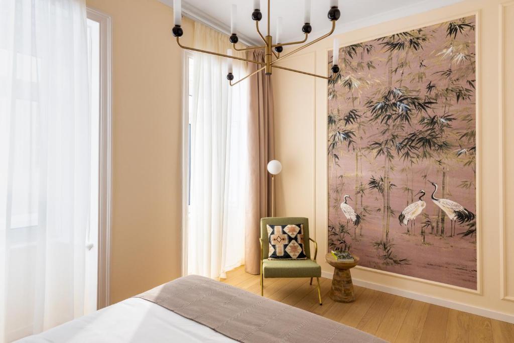 A bedroom with tall curtained windows, a green armchair, and large botanical wall art.