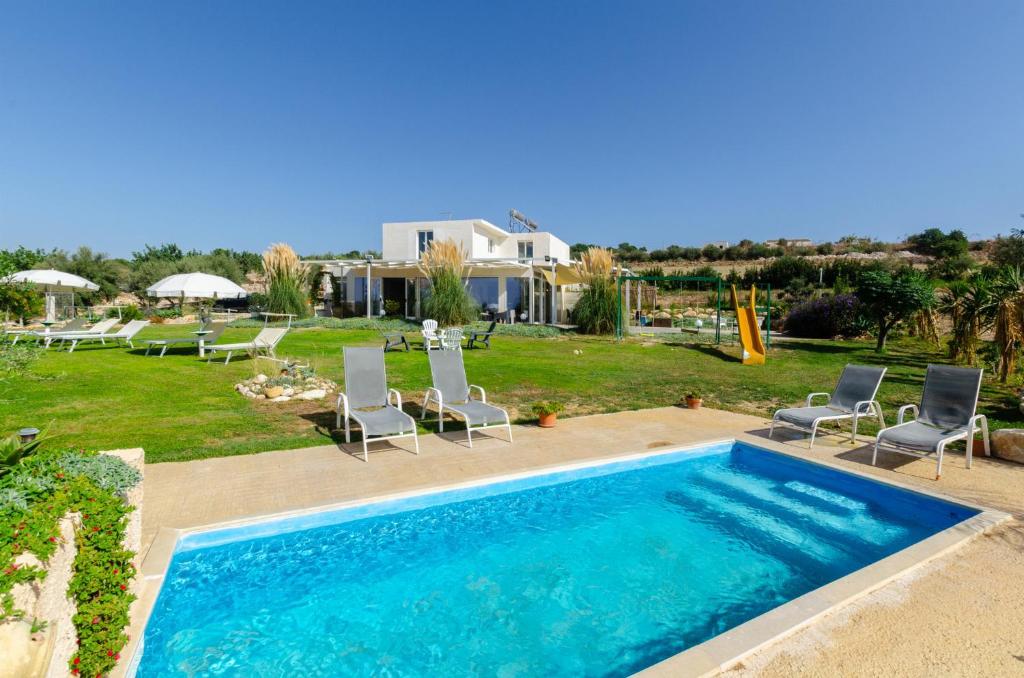 een zwembad met stoelen en een tuin met een huis bij Villa Padima in Scicli