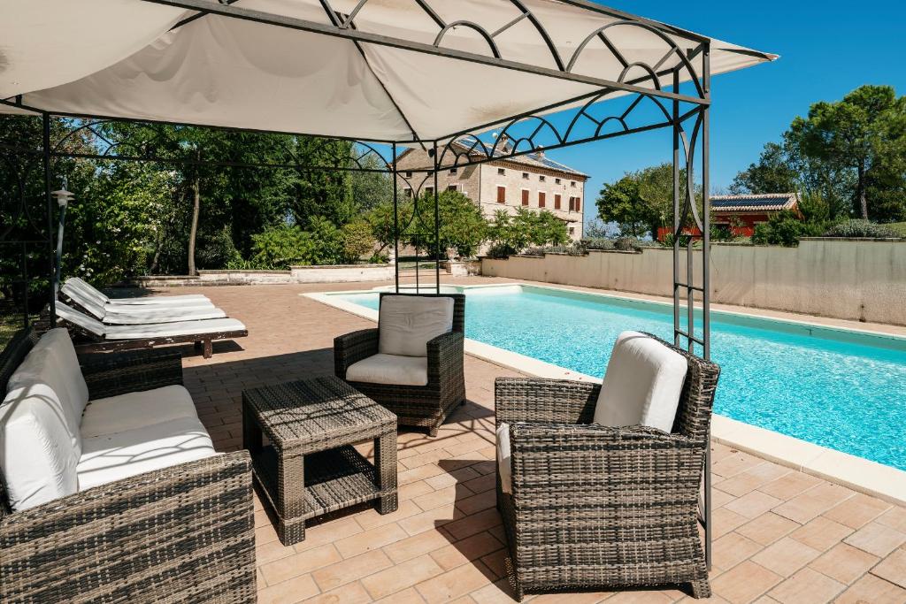eine Terrasse mit Stühlen und einem Sonnenschirm neben einem Pool in der Unterkunft Villa Maria by VacaVilla in Appignano