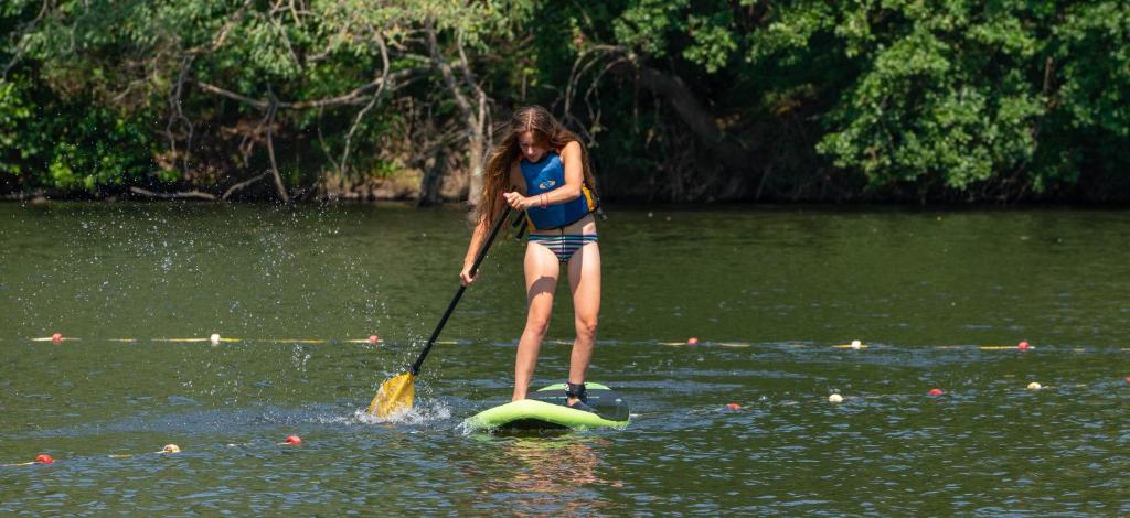 a woman standing on a paddle board in the water at Camping de la Bageasse in Brioude