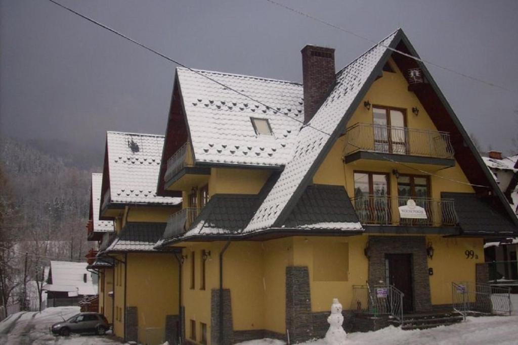 a yellow house with a black roof in the snow at TatroManiac Zakopane Pokoje in Zakopane