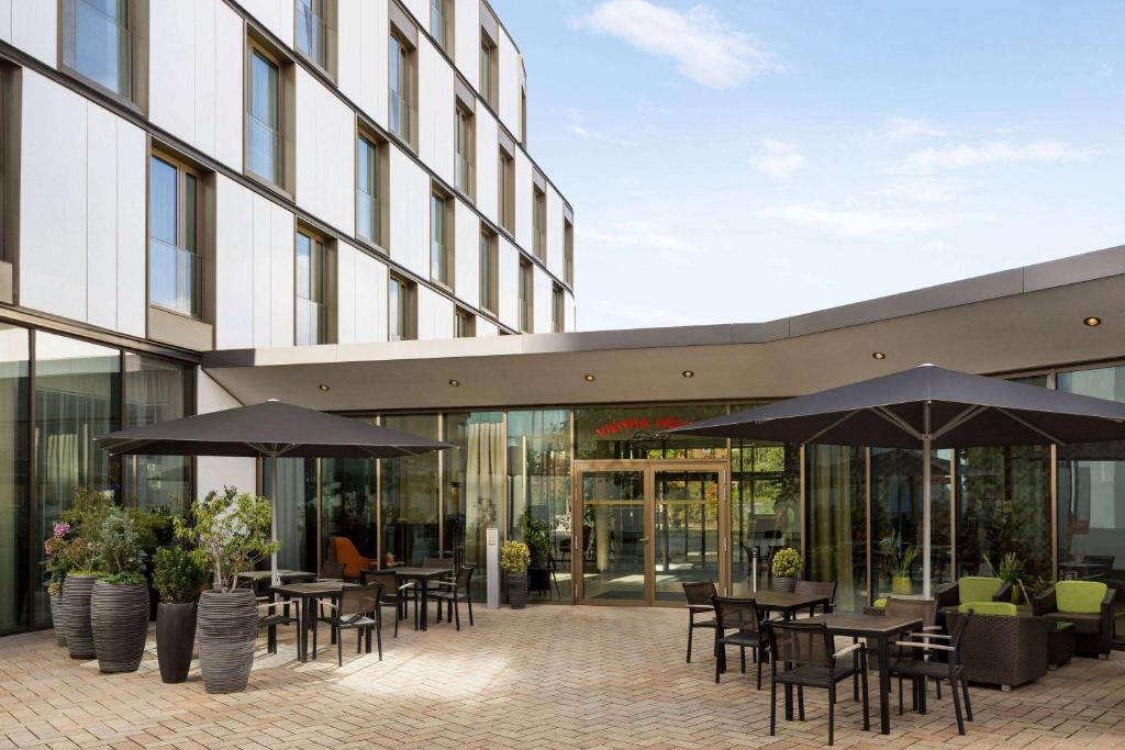 eine Terrasse mit Tischen und Sonnenschirmen vor einem Gebäude in der Unterkunft Vienna House Easy by Wyndham Osnabrück in Osnabrück