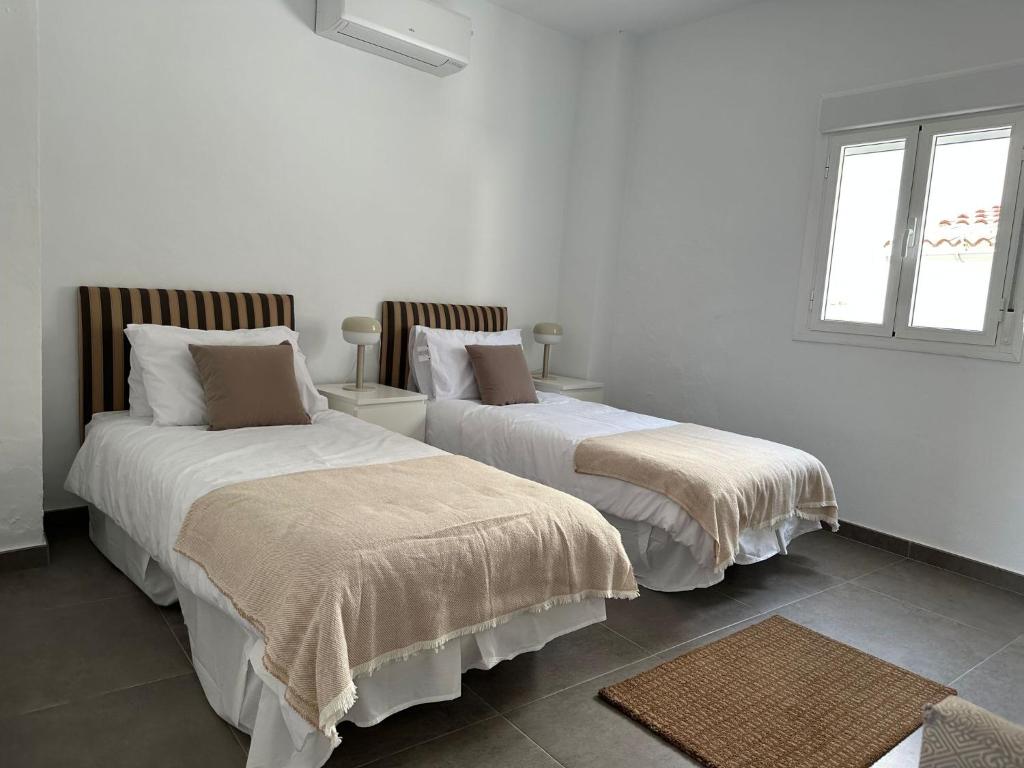 2 camas en una habitación con paredes y ventanas blancas en Heart of the Pueblo Townhouse, en Tolox