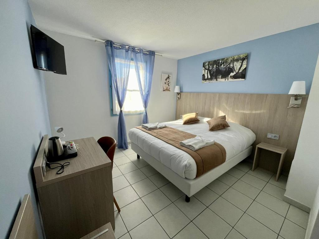 um quarto com uma cama, uma secretária e uma televisão em Hôtel Les Arcades em Saintes-Maries-de-la-Mer
