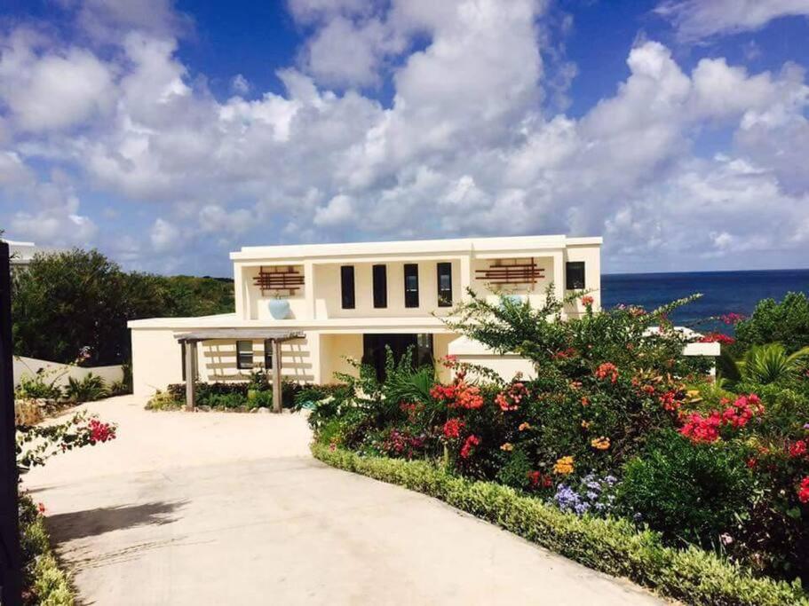 a white house with flowers in front of the ocean at Anguilla Sunset Beach House in Crocus Hill