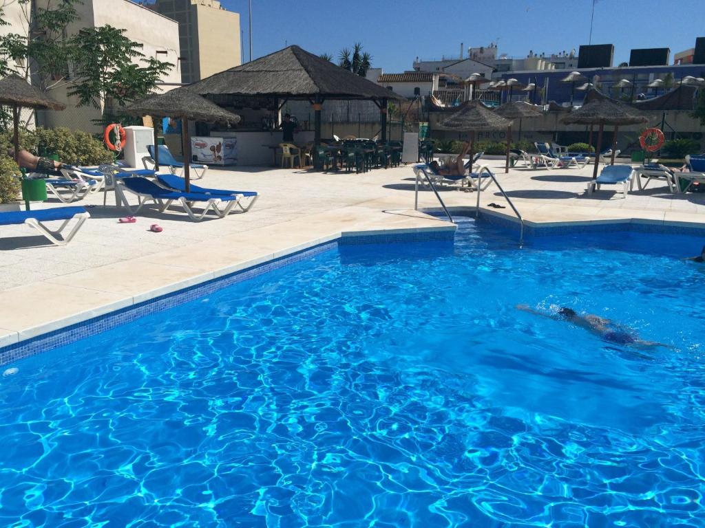 uma grande piscina azul com cadeiras e guarda-sóis em Apartamentos la Nogalera em Torremolinos