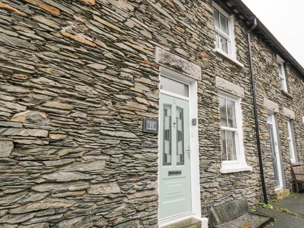 a stone house with a white door and a stone wall at St Mary's Cottage in Windermere