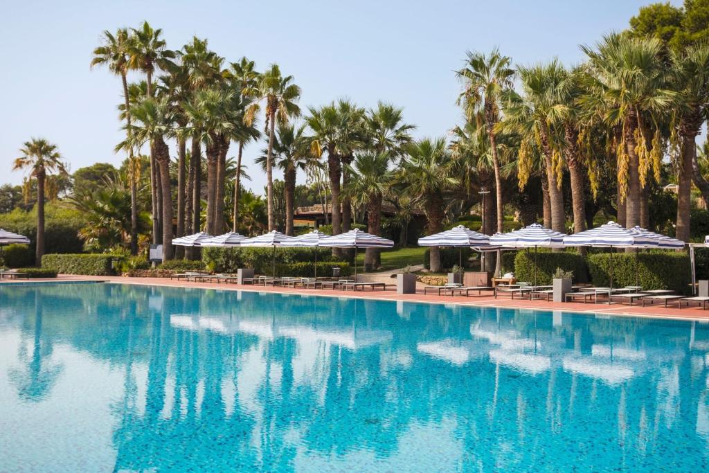 a pool at a resort with palm trees and umbrellas at Mangia's Brucoli, Sicily, Autograph Collection in Brucoli