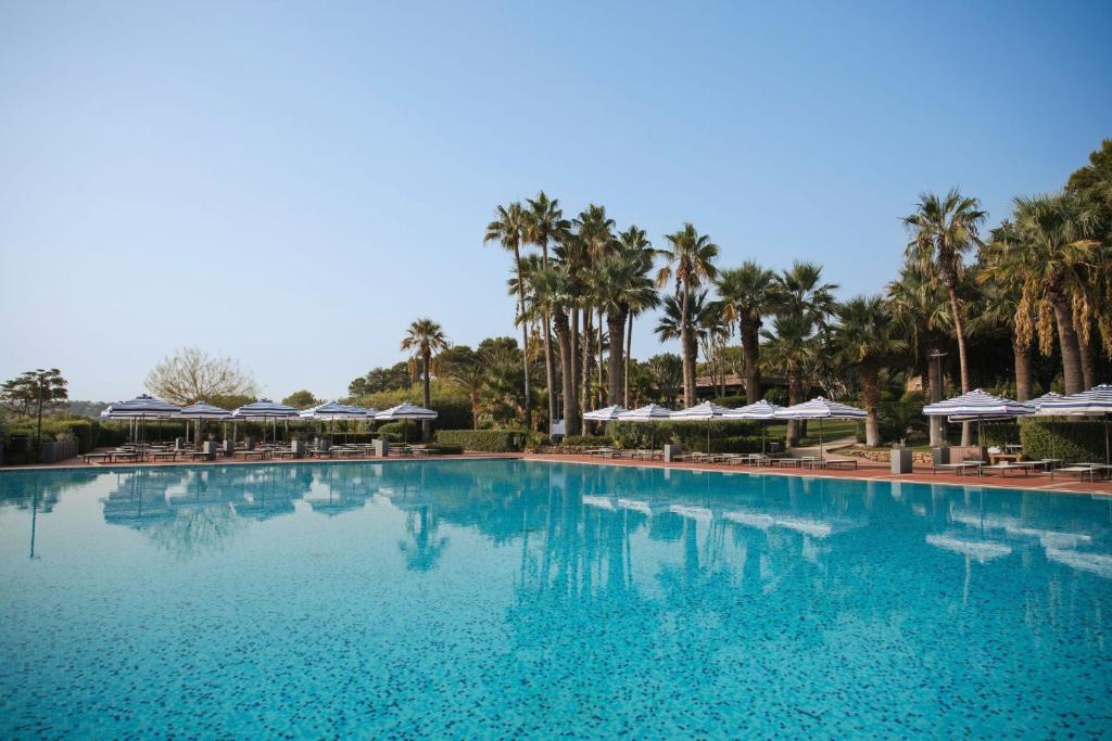 a large swimming pool with palm trees and umbrellas at Mangia's Brucoli, Sicily, Autograph Collection in Brucoli