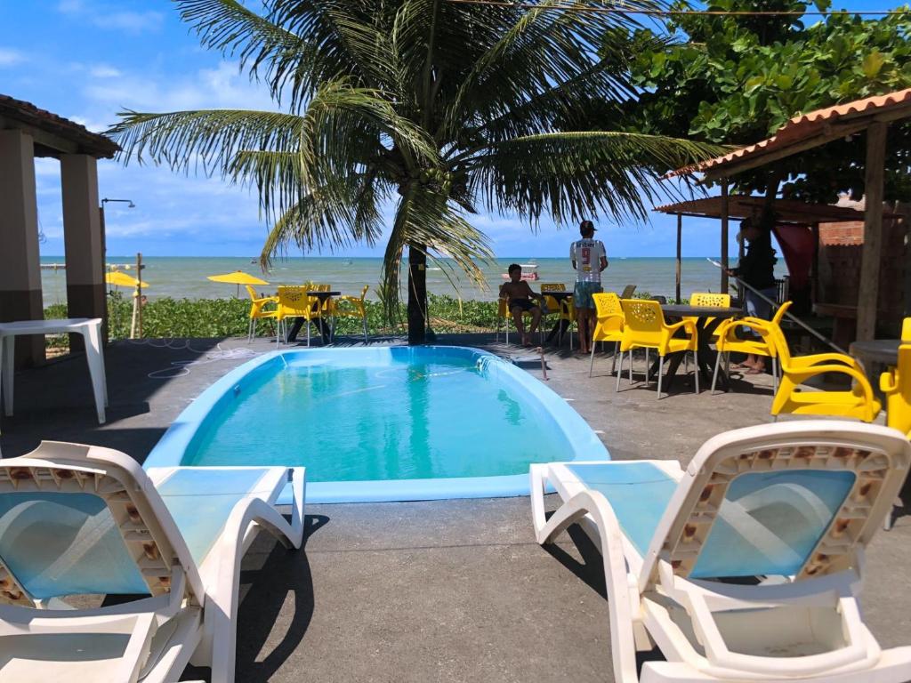 a swimming pool with chairs and a table and the ocean at Pousada e Restaurante Império do Marisco in Maragogi