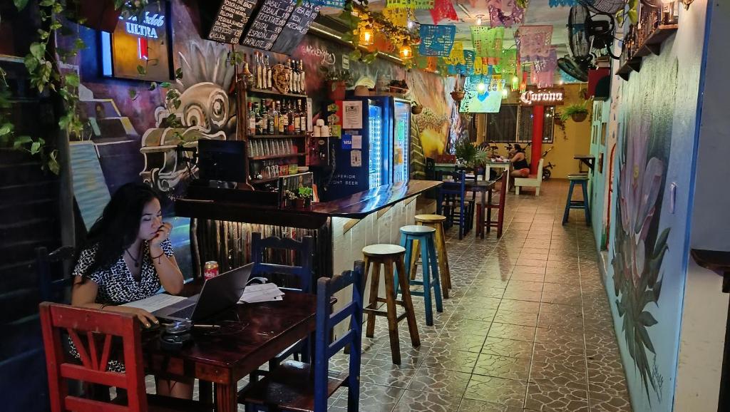 Eine Frau, die an einem Tisch in einer Bar mit einem Laptop sitzt. in der Unterkunft Tres Mundos Hostel in Playa del Carmen