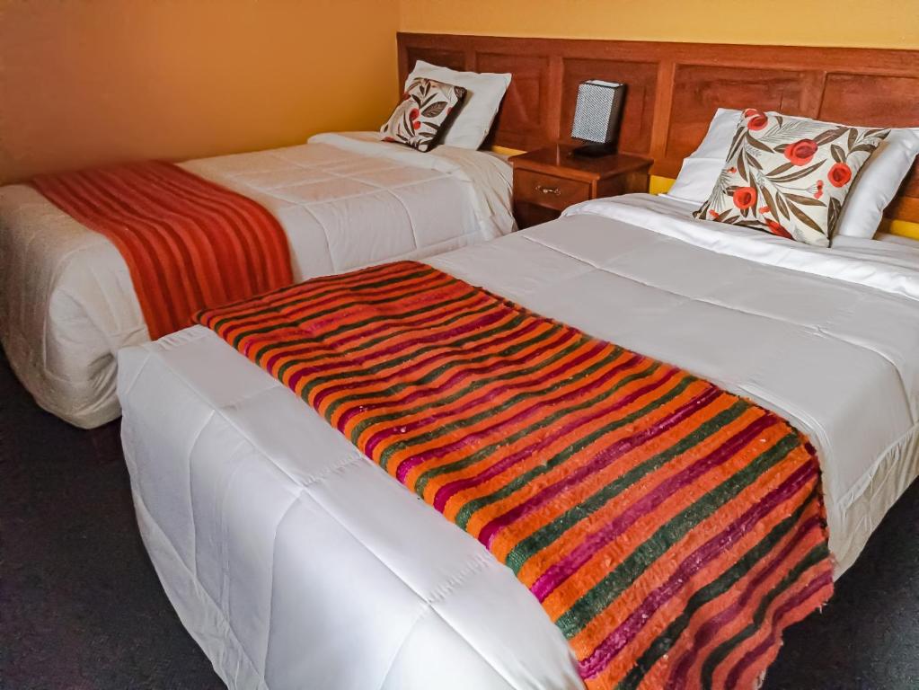 Dos camas en una habitación de hotel con una manta de colores. en Huaraz Center Hostal, en Huaraz