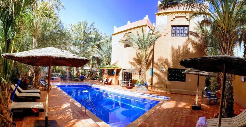 a swimming pool with umbrellas next to a building at Riad le petit jardin in Zagora