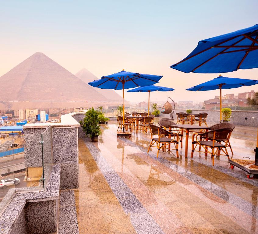 a patio with tables and blue umbrellas and the pyramid at Blue Pyramids Eyes Hotel in Cairo