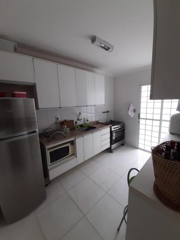 une cuisine avec des armoires blanches et un réfrigérateur en acier inoxydable dans l'établissement Casa Centro Caraguatatuba, à Caraguatatuba