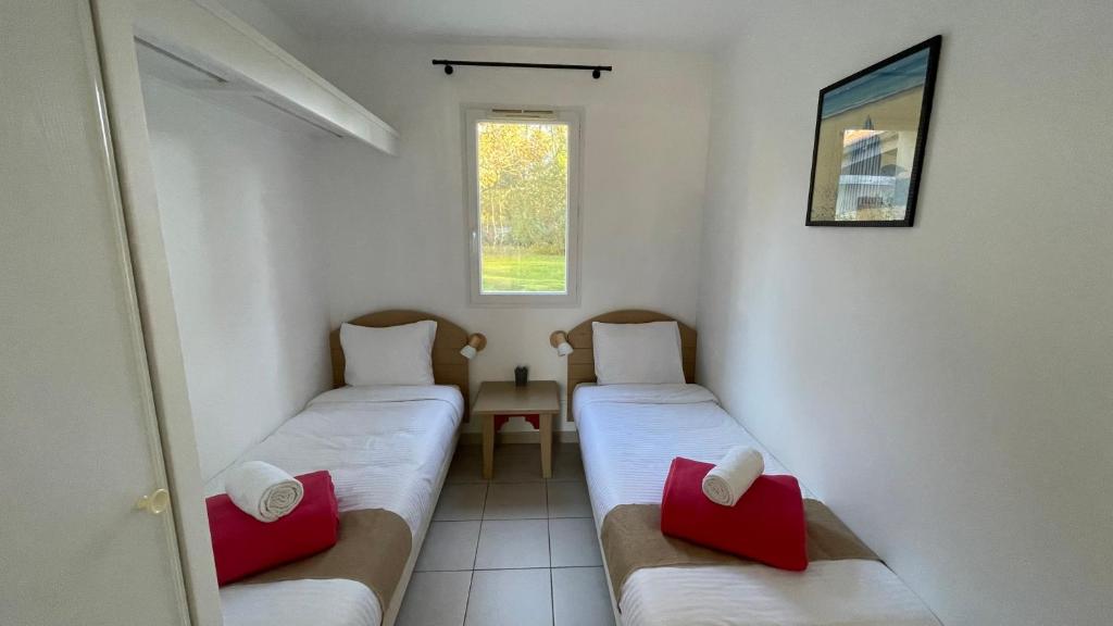 um pequeno quarto com 2 camas e almofadas vermelhas em Chalet paisible à la plage, piscine et tennis em Ondres