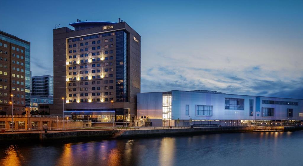 a tall building next to a river with buildings at Hilton Belfast in Belfast