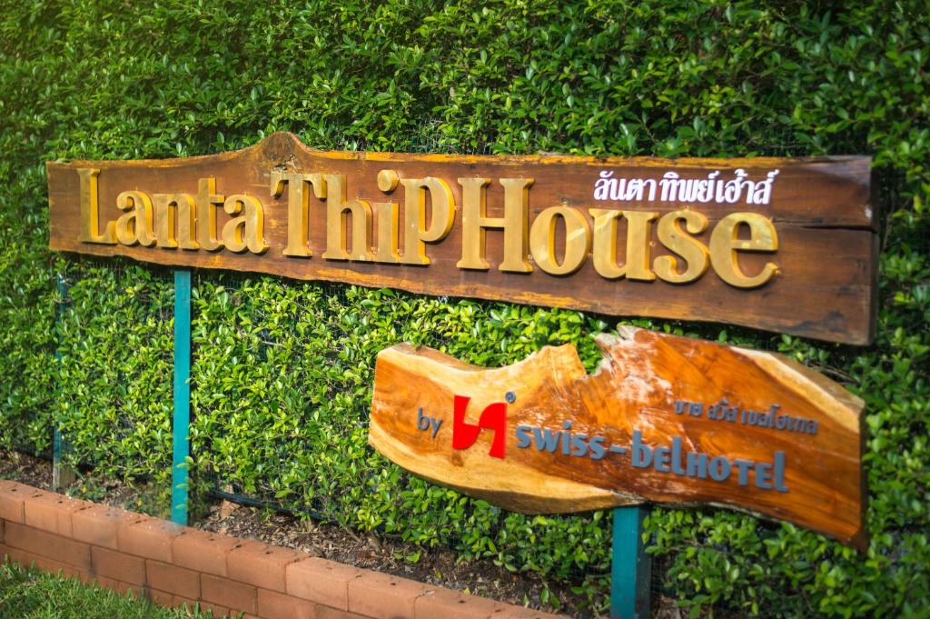 a sign in front of a bush with a house at Lanta Thip House by Swiss-Belhotel - SHA Plus in Ko Lanta