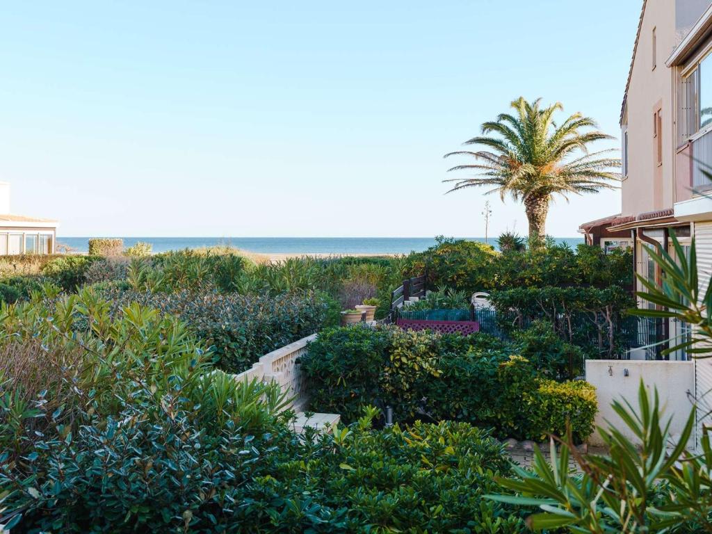 un jardin avec un palmier et un bâtiment dans l'établissement Appartement T3 avec terrasse, véranda et piscine, à 100m de la mer! Parking, animaux acceptés - FR-1-409-179, à Gruissan
