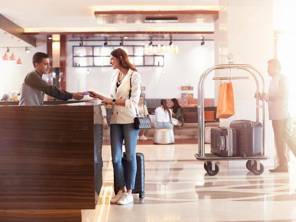 a woman standing at a counter in an airport with her luggage at Flora Al Barsha Hotel At The Mall in Dubai