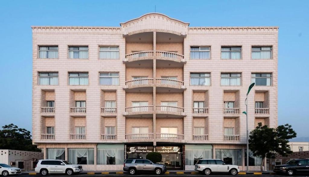 Dibba Sea View Hotel by AMA Pro في دبا: مبنى وردي فيه سيارات متوقفة أمامه