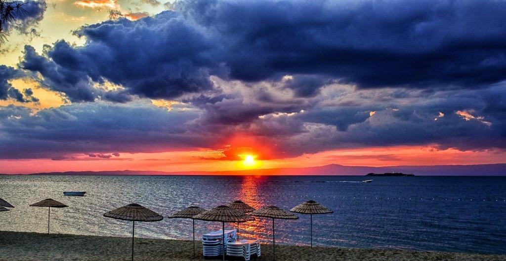 a sunset on a beach with umbrellas and the ocean at Calis Beach Random Rooms by LookBookHoliday in Fethiye