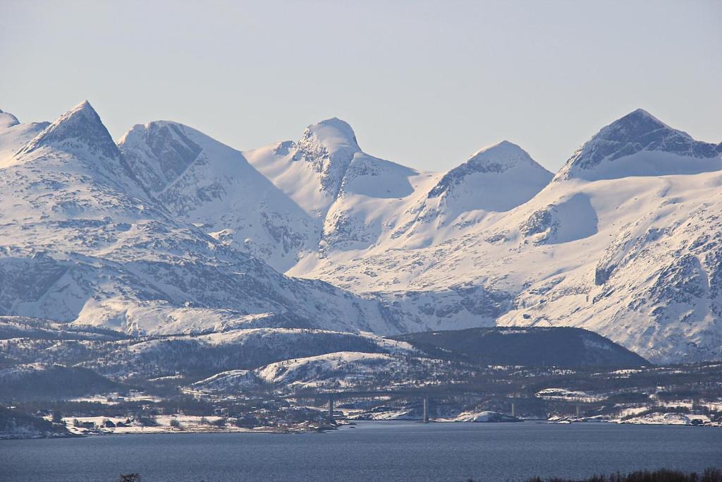 a snow covered mountain range with a body of water at Room in a house, with a nice view, in a quiet street in Bodø