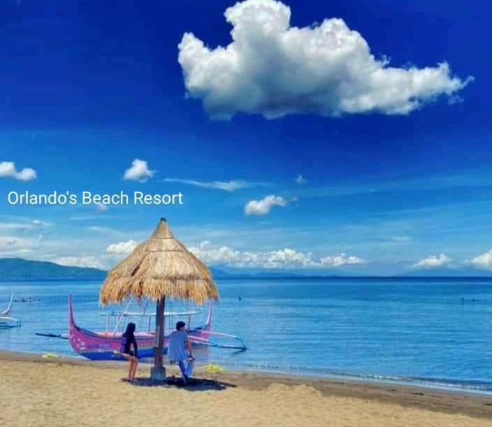 two people standing under an umbrella on a beach at Orlando Beach Resort in Lemery