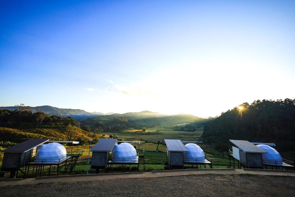 um grupo de cúpulas num campo com montanhas ao fundo em สวนไร่รุ่งอรุณ em Ban Na Pa Paek
