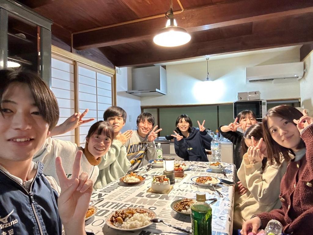 un grupo de personas sentadas alrededor de una mesa comiendo comida en Guesthouse ONE WORLD en Kitsuki