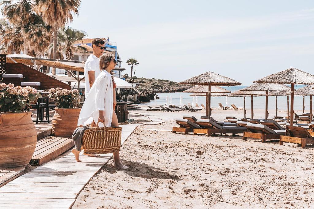 Almira Hotel في أركودي: رجل وامرأة يسيران على الشاطئ