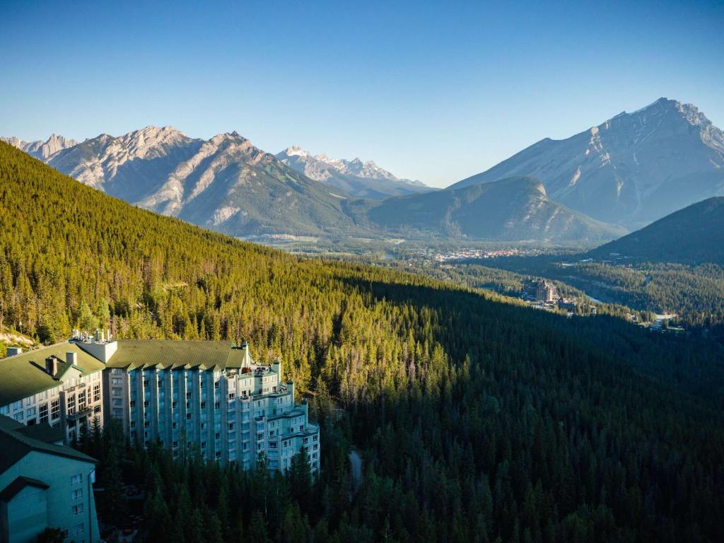 a building on a hill with trees and mountains at The Rimrock Resort Hotel Banff in Banff