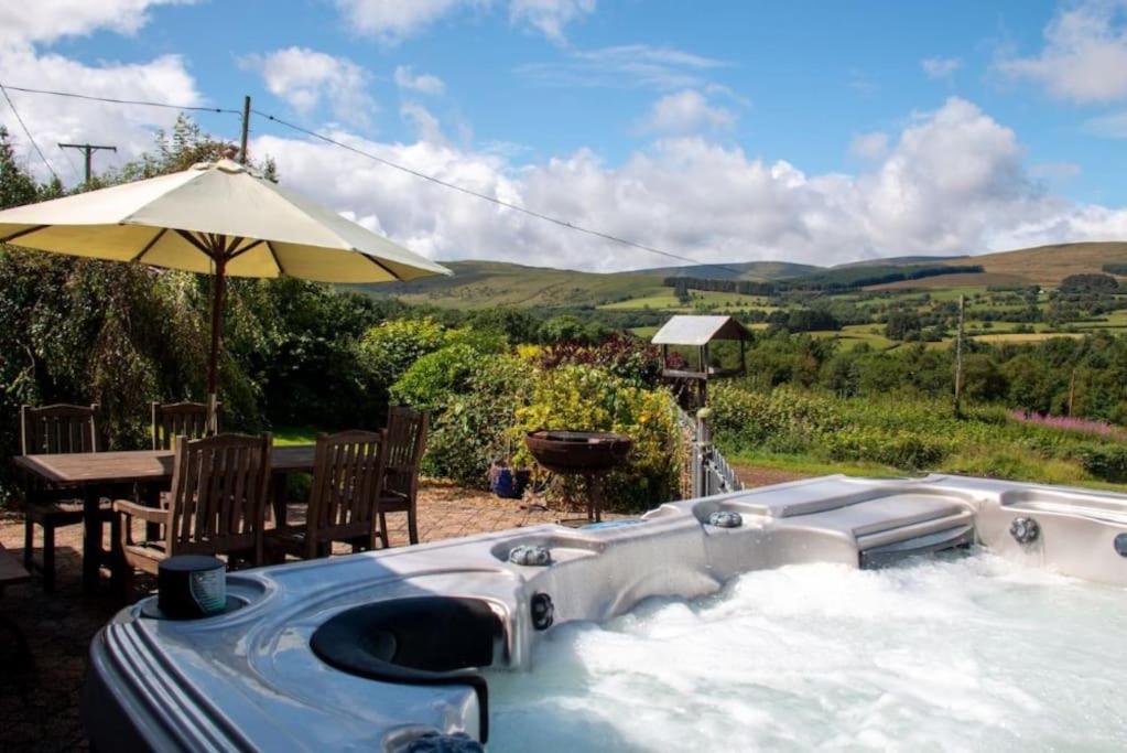 a hot tub with a table and an umbrella at Bedlwyncoch Farmhouse in Brecon