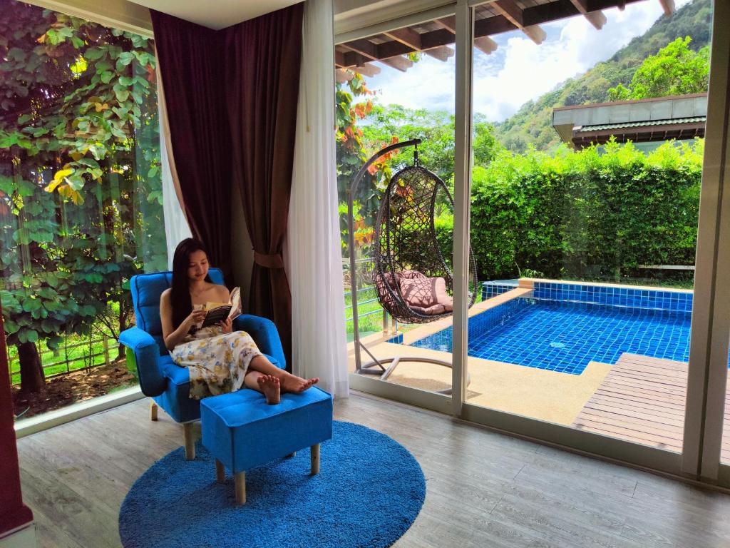 una mujer sentada en una silla azul leyendo un libro en Phuket Jungle Experience Resort en Karon