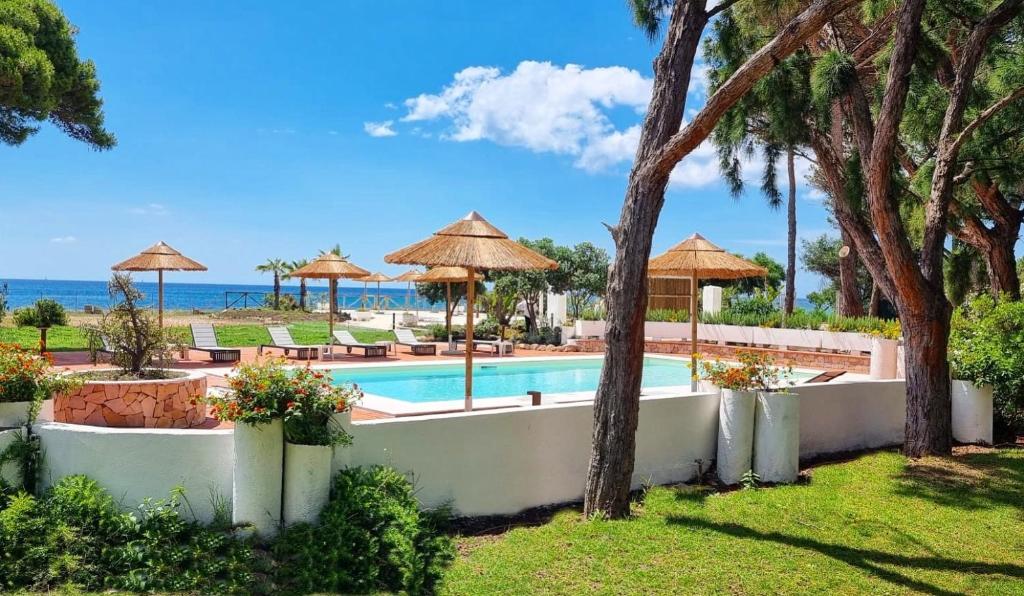 a swimming pool with umbrellas and the ocean at Hotel Mare Pineta in Santa Margherita di Pula