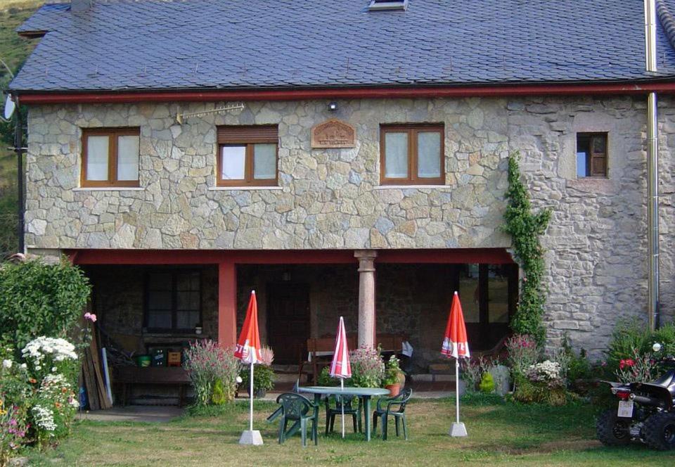 a stone house with a table and two red umbrellas at La Solana de Babia in Torrestío