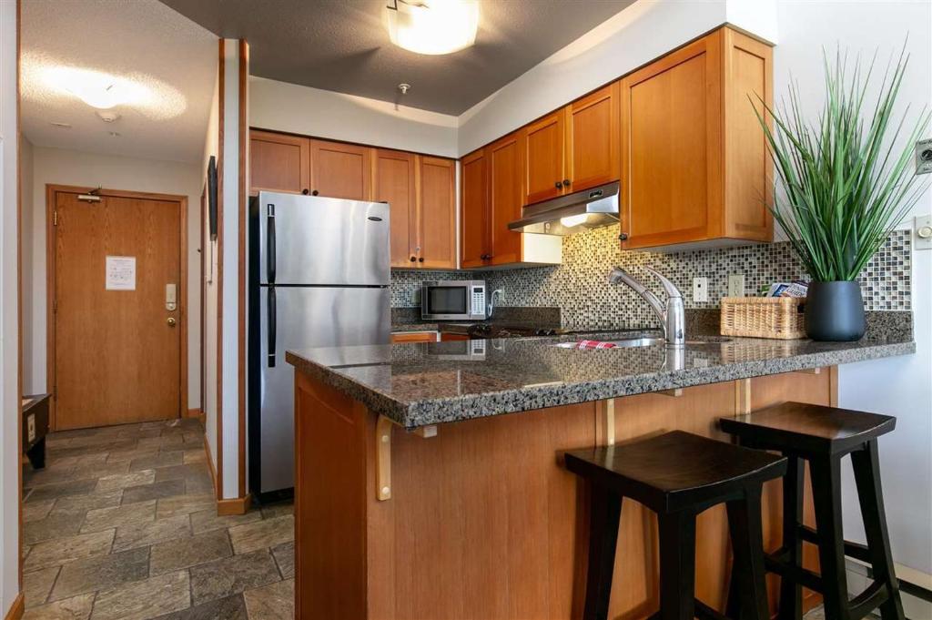 a kitchen with wooden cabinets and a stainless steel refrigerator at Bright 2 bedroom and loft suite in the Wildwood Lodge in Whistler