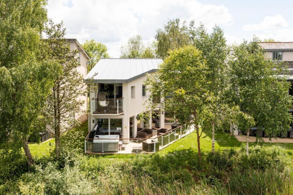 a house with a large porch and trees at Osprey Lodge CW64 HOT TUB Lakeside Spa Property in Somerford Keynes