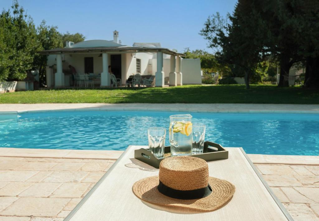 un chapeau et des lunettes sur une table à côté d'une piscine dans l'établissement Trulli La Formosa - The Fab Stay, à Ostuni