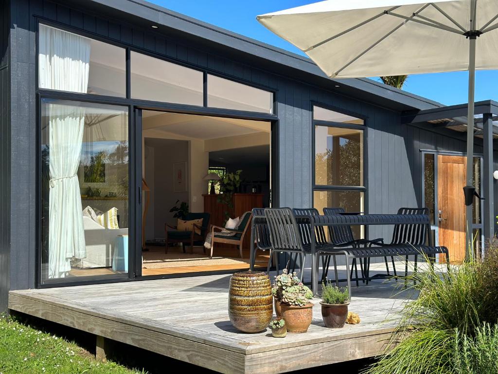 a house with a deck with chairs and an umbrella at The Driving Creek Cottage in Coromandel Town