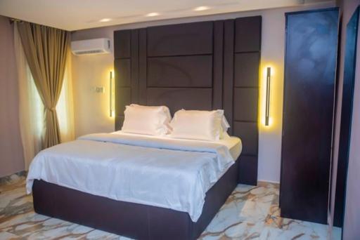 a bedroom with a bed with white sheets and pillows at Triple Tee Hotel & Service Apartments in Ikeja