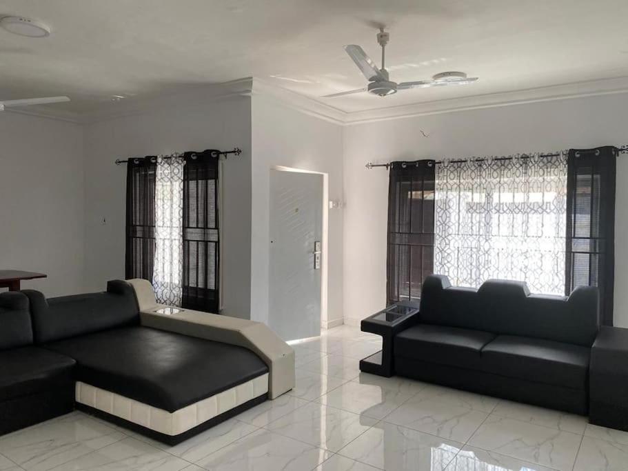 ein Wohnzimmer mit einem schwarzen Sofa und Fenstern in der Unterkunft Sigma Theta Homes - Old Tafo in Kumasi