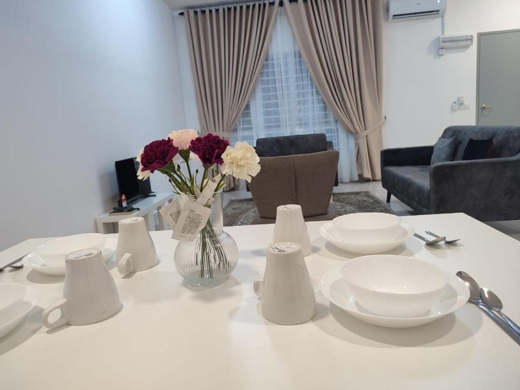 una mesa blanca con platos blancos y flores en un jarrón en Umi Homestay, Laman Haris, en Bandar Puncak Alam