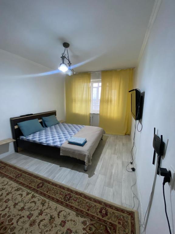 een slaapkamer met een bed en een televisie en een tapijt bij Уютные апартаменты в 11 микрорайоне (центр города) in Aqtöbe