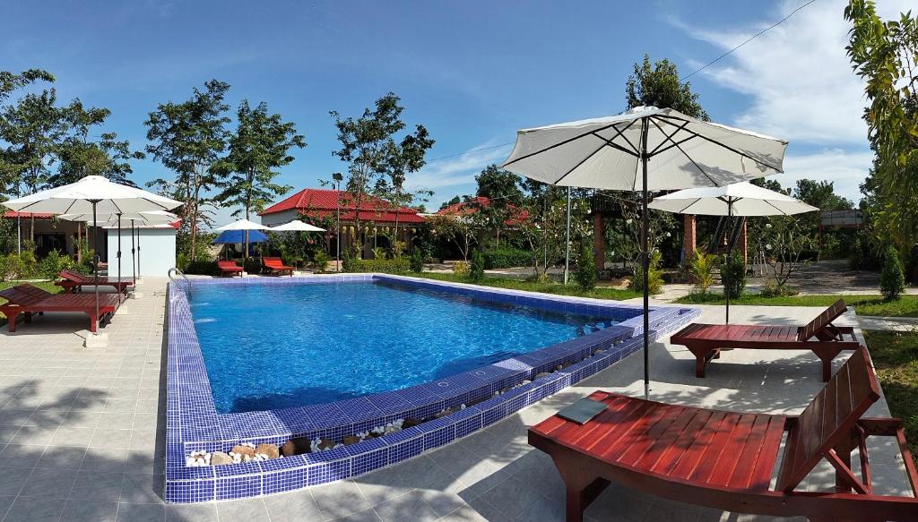 a swimming pool with two benches and umbrellas at Kampot Nature Villa Resort in Kampot