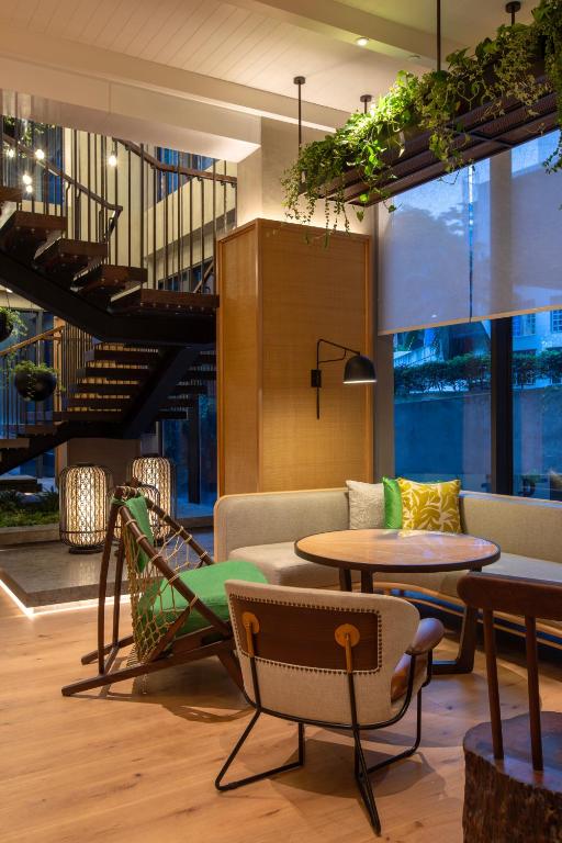 A compact lobby seating nook framed by a staircase, windows, and hanging plants.