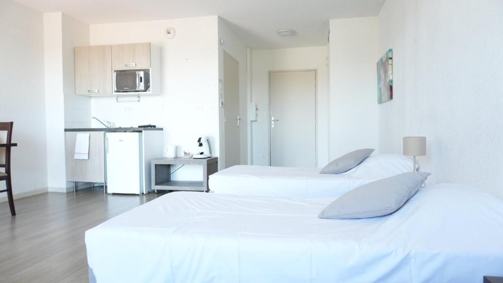 two beds in a white room with a kitchen at Zenao Appart's Yzeure in Yzeure