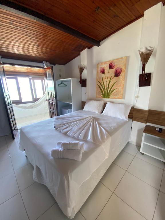 a bedroom with a white bed with a painting on the wall at Pousada Maramar/terceira praia MSP in Morro de São Paulo